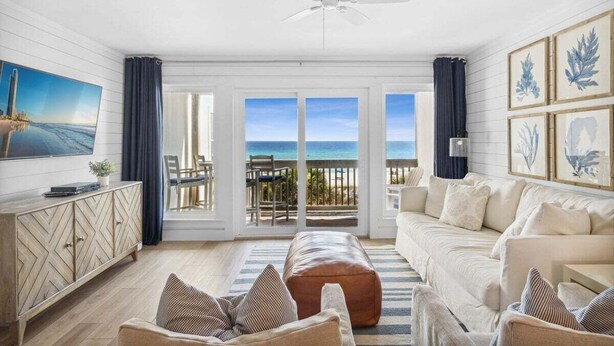Ein geräumiges Wohnzimmer mit großem Fenster zum Meer, einem Deckenventilator und einer Holzkommode.