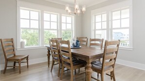 Une salle à manger avec une table et des chaises en bois, de grandes fenêtres et un lustre.