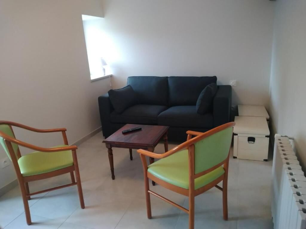 A living room with a black sofa, two wooden chairs with green cushions, a small wooden table, and a white cabinet.