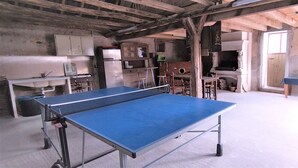 A spacious room with a ping pong table, wooden cabinets, and a rustic ceiling. - Gîte de la Basse Roche (Souge)