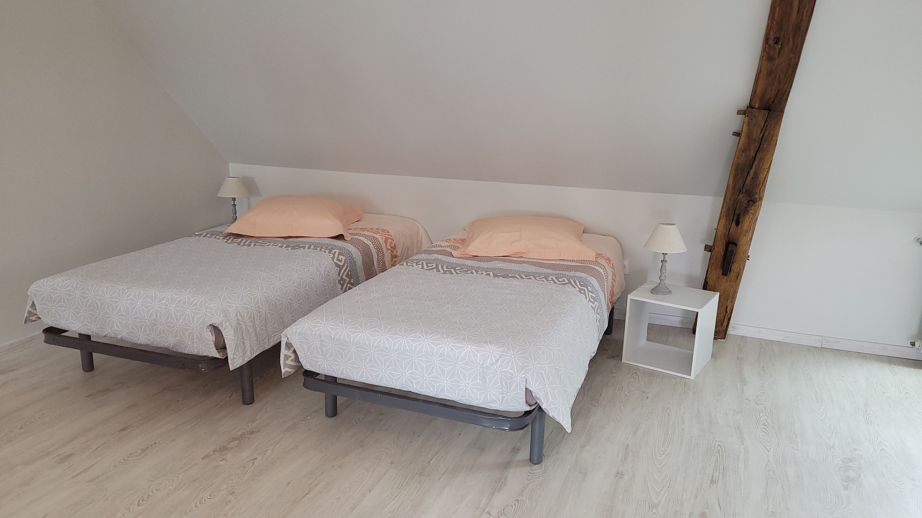 A bedroom with two beds, each with a patterned bedspread and matching pillows. There is a nightstand with a lamp on one side.