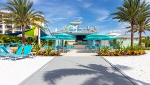 Ein Steg führt zu einer Bar und einem Grillrestaurant namens Salty Rim, mit türkisfarbenen Sonnenschirmen und Liegestühlen an beiden Seiten.