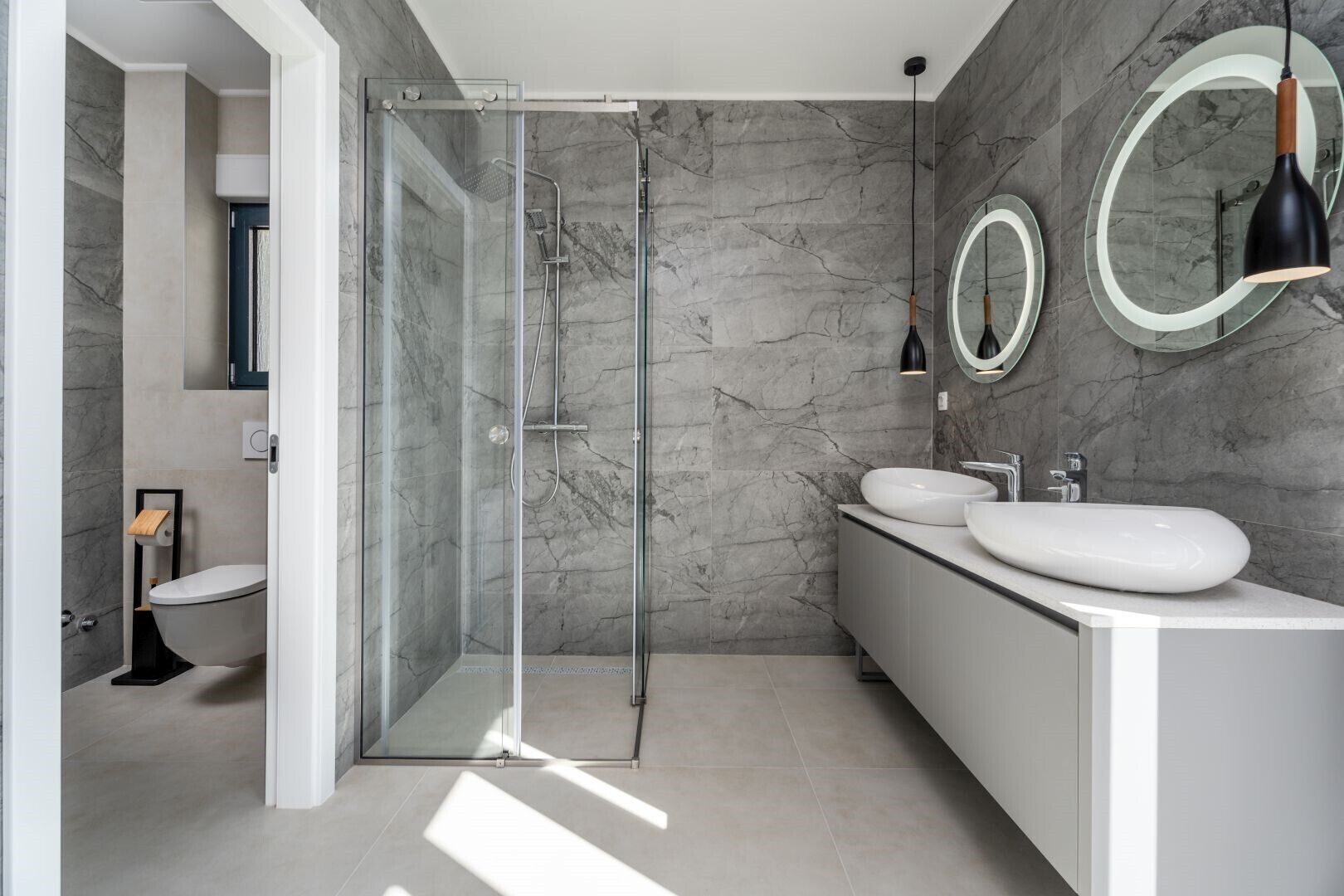 Ein modernes Badezimmer mit einer Glasdusche, zwei Waschbecken und Marmorwänden.