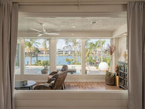 A room with a large window, a ceiling fan, wicker furniture, and a view of a pool and palm trees.