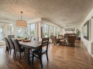 A spacious dining area with a large wooden table, dark chairs, and a hanging light fixture. - Waterfront Oasis - King Beds • 10min Walk to Beach (Cocoa Beach)
