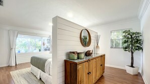 A bedroom with a wooden dresser, a bed, a large mirror, and a potted plant. - Waterfront Oasis - King Beds • 10min Walk to Beach (Cocoa Beach)
