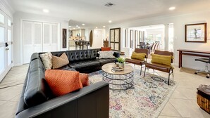A spacious living room with a black leather sofa, a round coffee table, and a patterned rug. There is a dining area with a wooden table and chairs visible in the background. - Waterfront Oasis - King Beds • 10min Walk to Beach (Cocoa Beach)