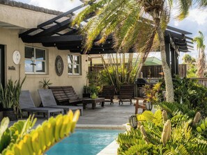 Un espace aménagé au bord de la piscine, avec des chaises longues, une pergola et diverses plantes.