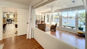 A spacious room with a large window overlooking a pool and water view, wooden flooring, and a dining area with chairs and a table. - Waterfront Oasis - King Beds • 10min Walk to Beach (Cocoa Beach)