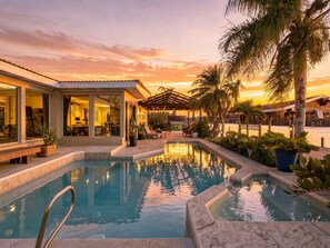 A pool area with a sunset view, a covered seating area, and a building with large windows.