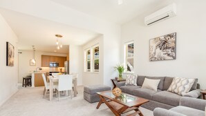 Un salon moderne avec un canapé gris, une table basse et un coin repas comprenant une table et des chaises blanches.