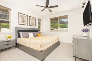 A bedroom with a bed, bedside tables, a ceiling fan, and large windows with a view.