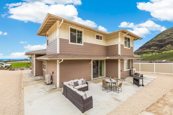 A two-story house with a covered patio area, outdoor furniture, and a grill.
