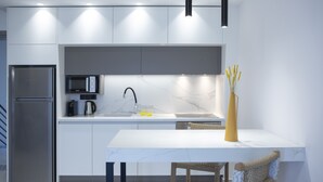 A modern kitchen with a stainless steel refrigerator, a microwave, and a sink. There is a white marble countertop and a yellow vase with yellow flowers. - Achillion Suites (Lefkada)