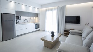 A modern kitchen with built-in appliances, a dining area with a minimalist table, and a living room with a sofa and TV. - Achillion Suites (Lefkada)
