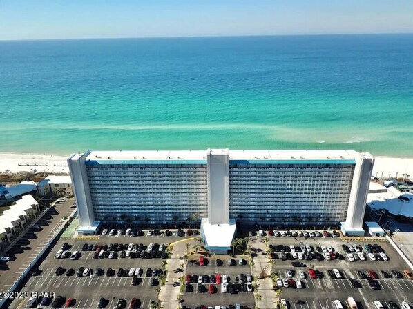 A large hotel with a parking lot in front, overlooking a beach and the ocean.