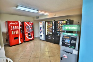 Eine Reihe von Getränkeautomaten verschiedener Marken, darunter Coca-Cola und Red Bull, in einem mit Fliesen ausgelegten Raum.