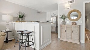 Une cuisine moderne avec des meubles blancs, un îlot central doté de tabourets, un miroir rond et un petit meuble contenant un panier en osier.