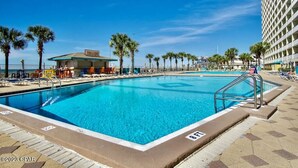 Une piscine avec un poste de surveillance pour les sauveteurs, des palmiers et, au fond, un bâtiment sur lequel on peut lire l’inscription « THIN BAR ».