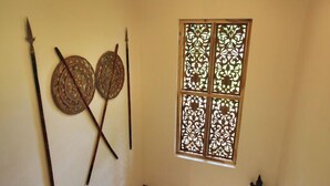 A room with a traditional window with intricate lattice design, a wooden floor, and two circular woven mats on the wall. - Far Horizons Villa by Angel (Unawatuna)