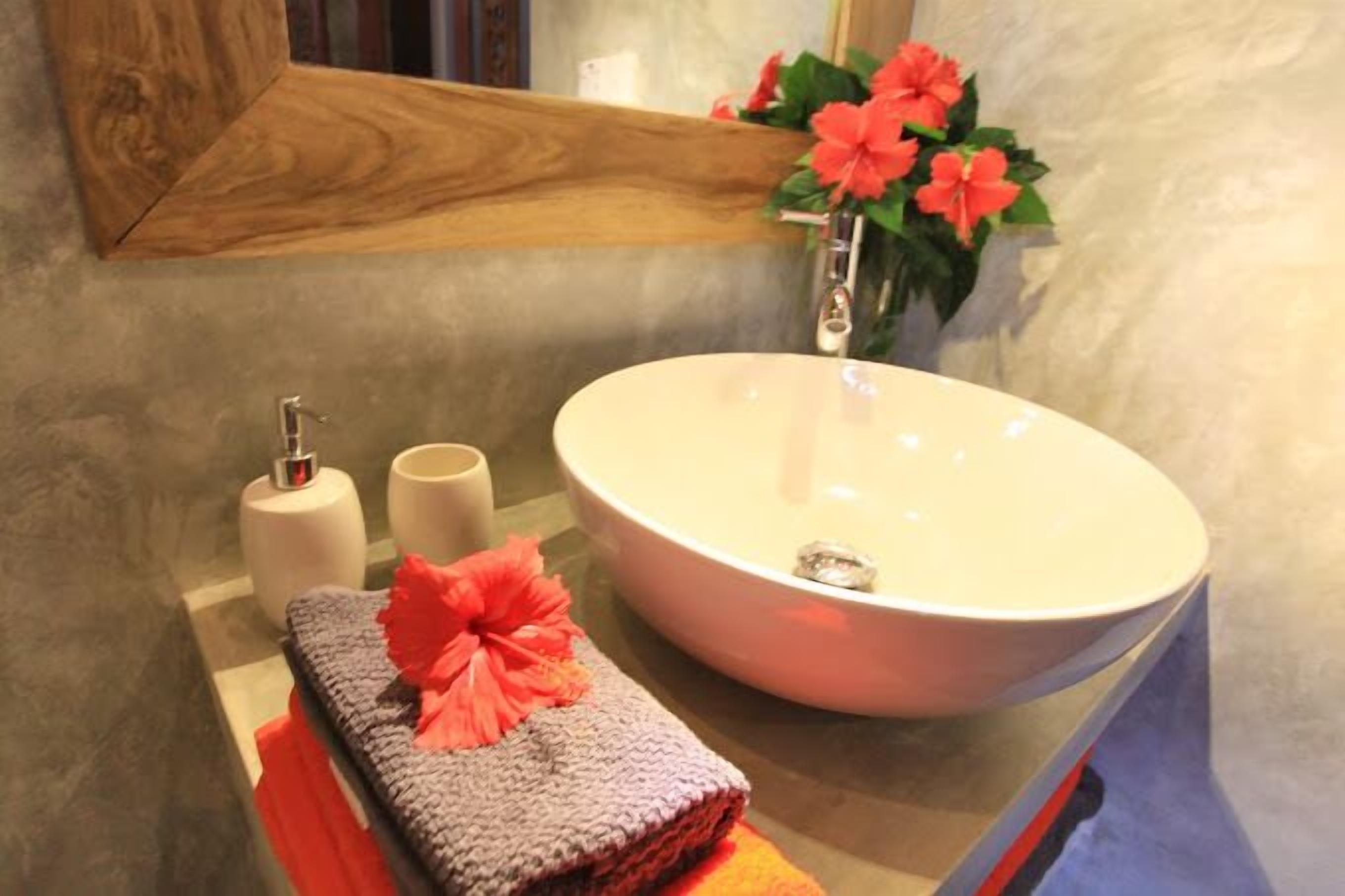 A bathroom with a white sink, two white toilet paper rolls, a towel with a red flower, and a vase with red flowers.