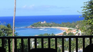 A view from a balcony overlooking a beach with a small building on a hill. - Far Horizons Villa by Angel (Unawatuna)