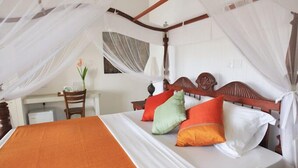 A four-poster bed with white and orange bedding, a desk with a chair, and a vase with a flower. - Far Horizons Villa by Angel (Unawatuna)