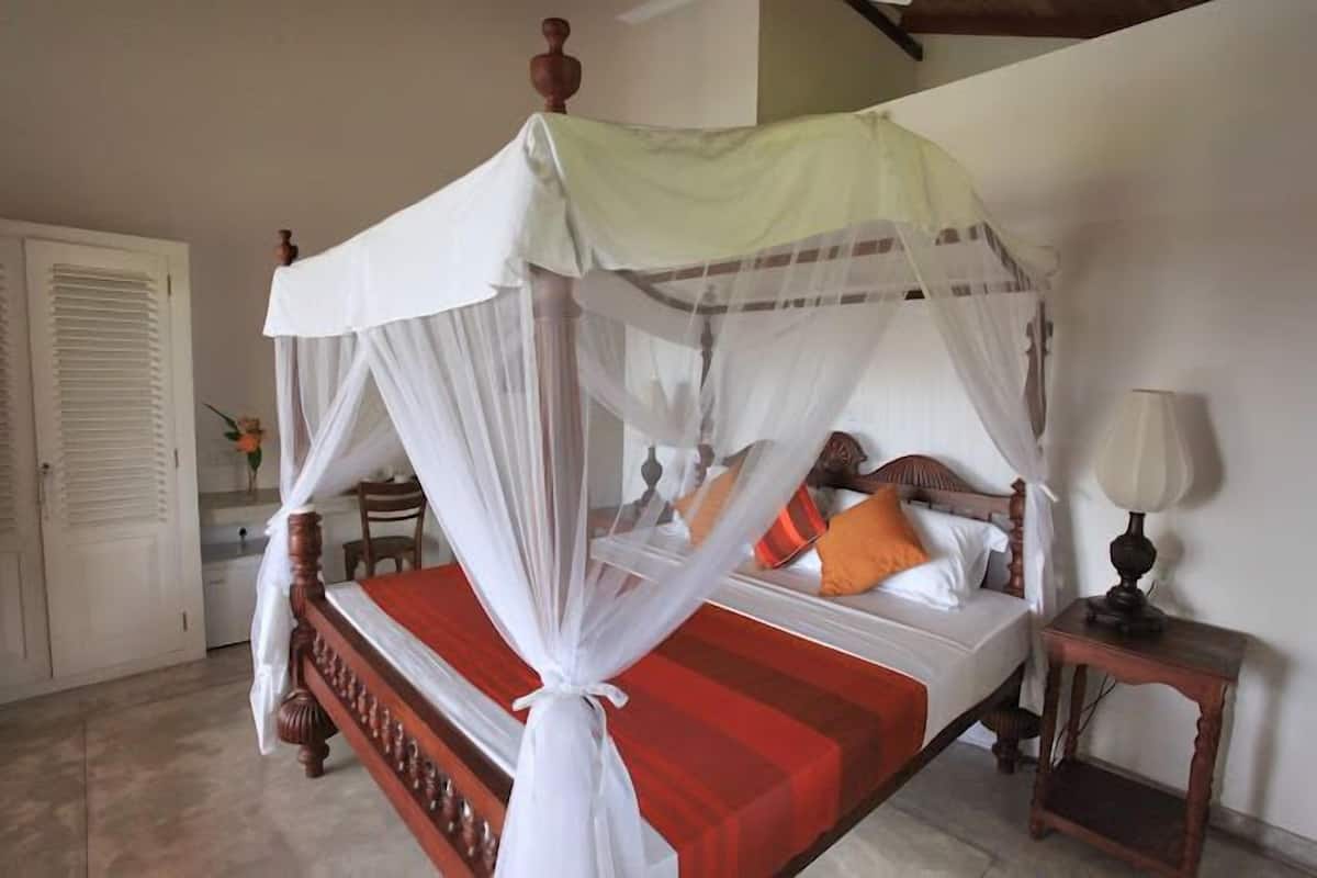 A four-poster bed with a canopy, a bedside table with a lamp, and a small table with a vase of flowers.