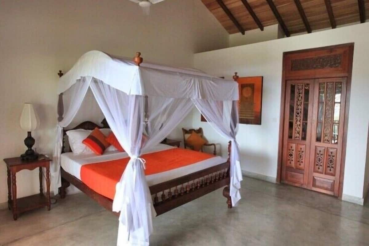 A four-poster bed with a canopy, a wooden nightstand with a lamp, and a traditional wooden door.