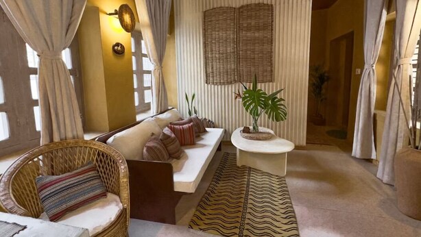 Una habitación acogedora con sofá, una silla de mimbre, una mesita y una planta en maceta.