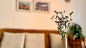 Un jarrón color beige con flores secas sobre una mesa en una habitación con un sofá color beige y dos cuadros en la pared.