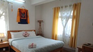 Un dormitorio con cama de madera, una mesita de noche, una lámpara, una pequeña mesa, una silla, una ventana con cortinas y un adorno en la pared.