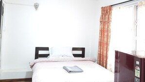 Un dormitorio sencillo y bien iluminado con cama, dos mesitas de noche, un armario y ventana con cortinas.