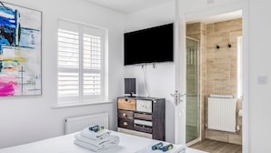 Una camera da letto con un letto, una televisione, una finestra con persiane, una porta che conduce al bagno e un quadro appeso al muro.