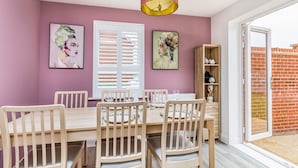 Zona pranzo con tavolo e sedie in legno, parete rosa e due quadri.