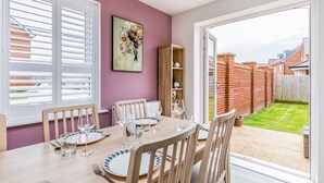Zona pranzo con tavolo imbandito per quattro persone, una libreria e vista su un muro in mattoni e un giardino tramite una porta vetrata.