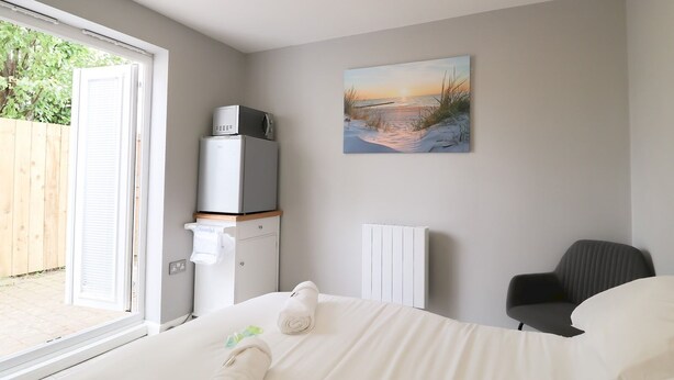 A bedroom with a bed, a radiator, a chair, and a painting of a sunset over water. - Modern Room with Private Outdoor space - Pass the Keys (Newcastle)