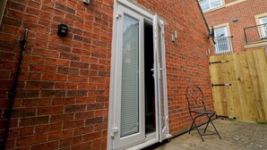A brick house with a white-framed door, a wooden fence, and a metal chair. - Modern Room with Private Outdoor space - Pass the Keys (Newcastle)