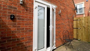A brick building with a white-framed door and a small outdoor seating area. - Modern Room with Private Outdoor space - Pass the Keys (Newcastle)