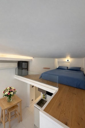 A compact room with a bed, a small table with a vase of flowers, and a kitchenette area. - Studio Neuf au Cœur du Carré Dor, rue Dalpozzo, 5 Minutes des Plages (NICE)