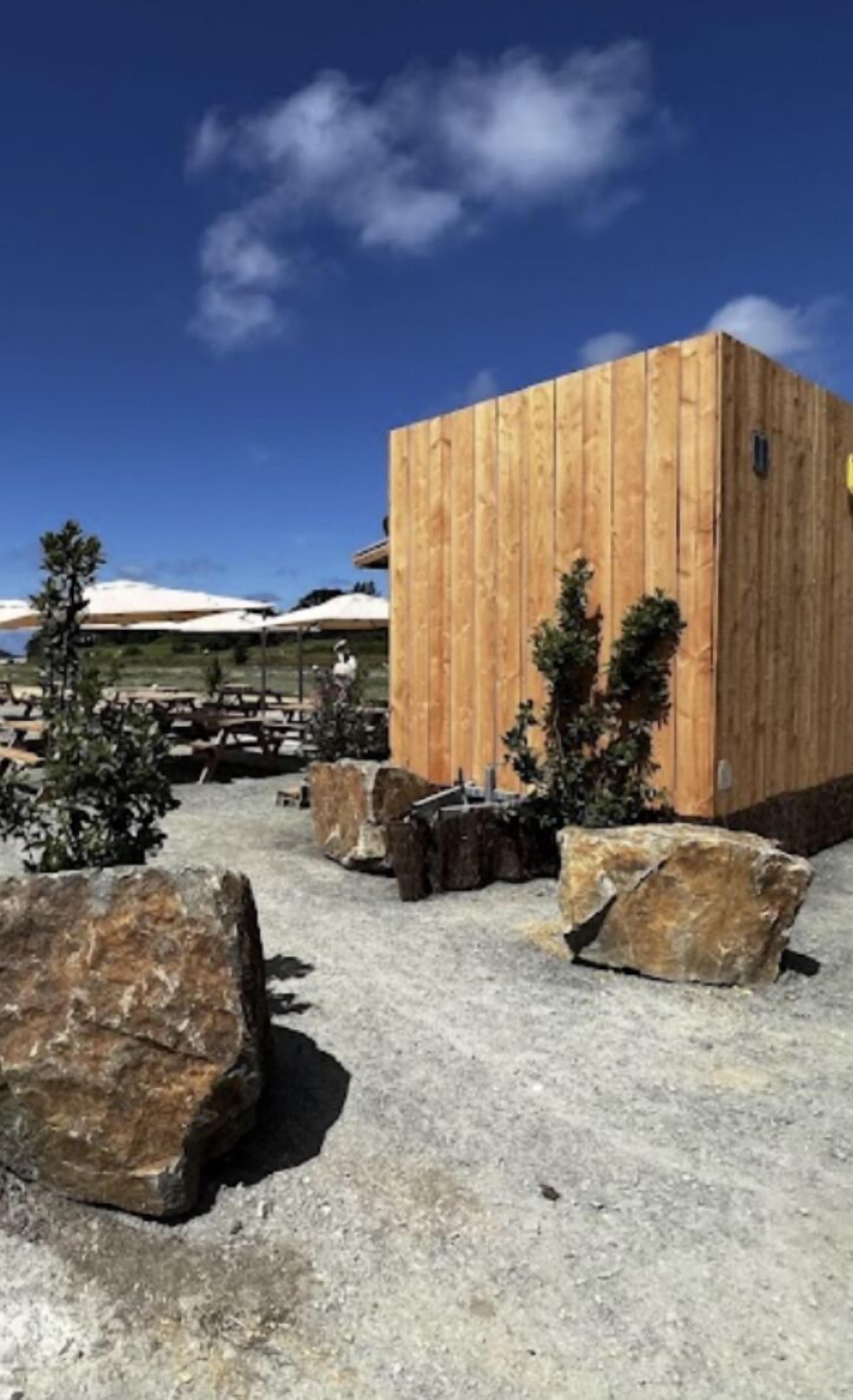 A modern wooden building with a flat roof, surrounded by large rocks and small trees.