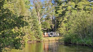 Un camping tranquilo para vehículos recreativos a orillas de un río sereno, rodeado de un bosque denso.