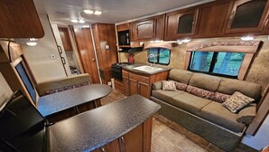 Cocina compacta para camper con armarios de madera, microondas, pileta y sofá con cojines estampados.