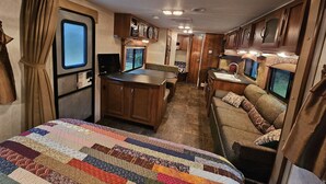 Interior compacto de una caravana con kitchenette, comedor y litera.