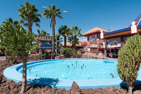 A pool area with palm trees, a building with a blue tiled roof, and a sign that reads "OPEN EVERY RIGHT".