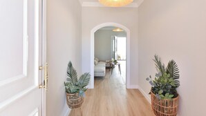 Un pasillo con suelo de madera, paredes blancas y un aplique de techo. Hay dos plantas en macetas a cada lado del pasillo.