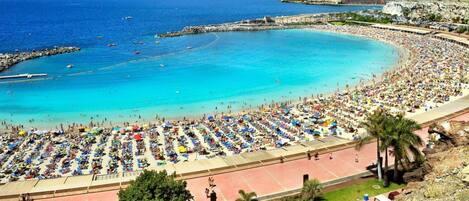 A crowded beach with numerous umbrellas and people enjoying the sunny weather.