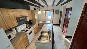A kitchen with wooden cabinets, a white stove, a sink, and a dining area with a table and chairs. - Cozy 3BR Beach House by the Sea (Old Orchard Beach)