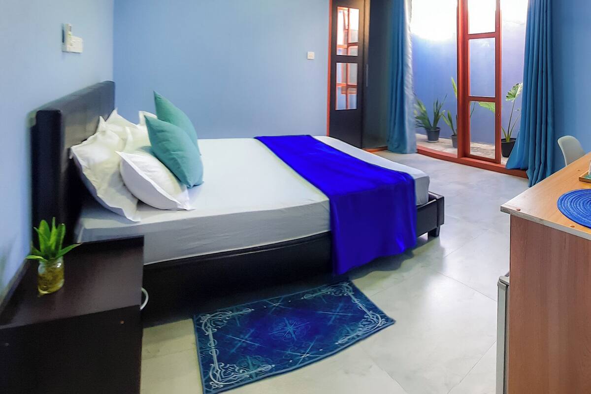 Un dormitorio con cama, escritorio, ventilador de techo y ventana con cortinas.