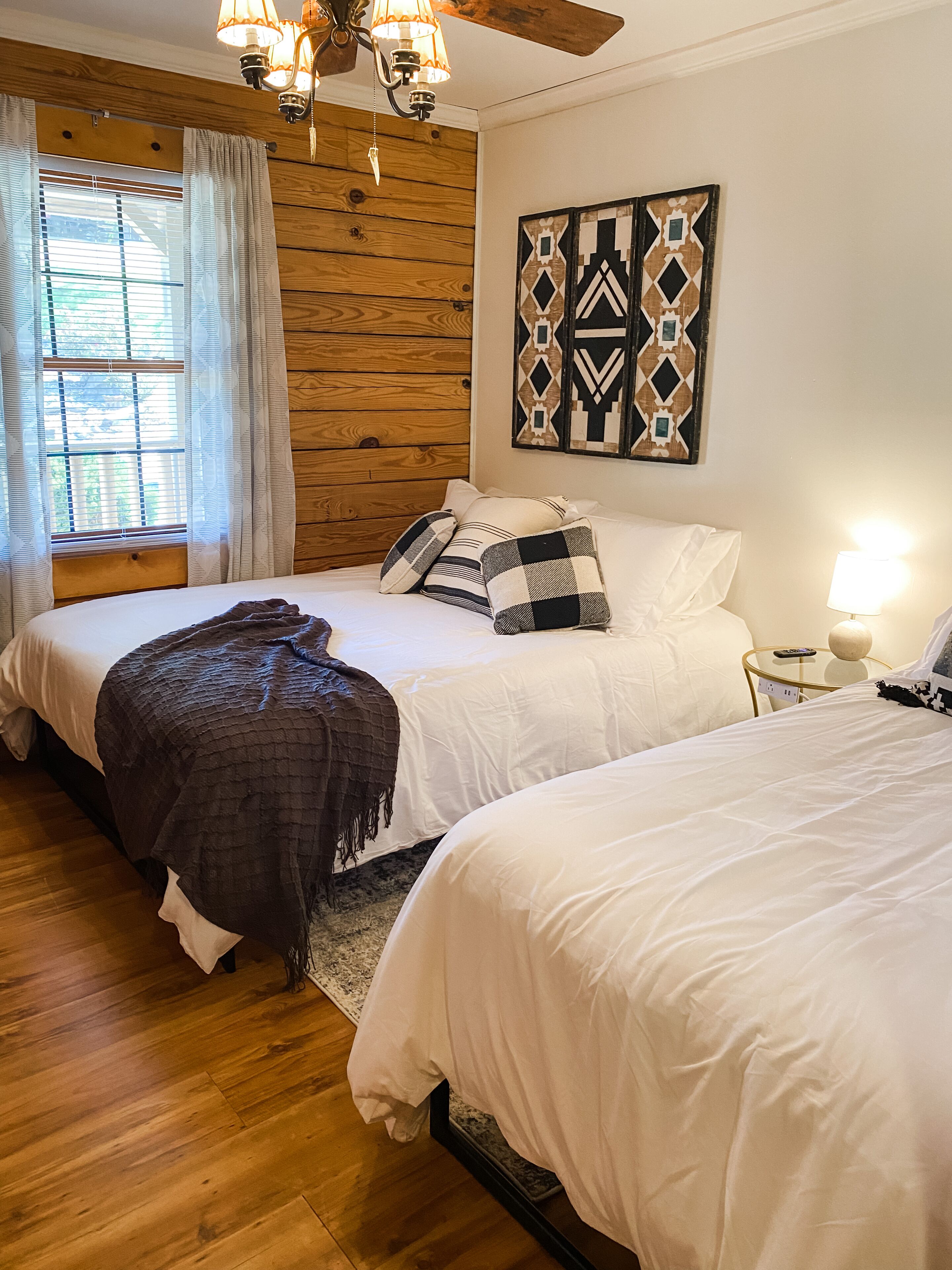 Une chambre avec deux lits, un lambris en bois, une décoration murale à motifs et une fenêtre avec des rideaux.